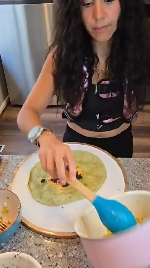 Crystal spreading filling across a large spinach tortilla with a spatula