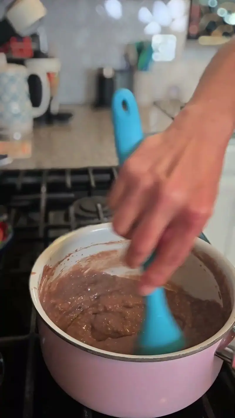 Stirring chocolate protein oatmeal in a pink saucepan on the stove