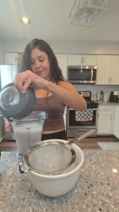 Crystal straining the blended milk through a sieve into a white bowl