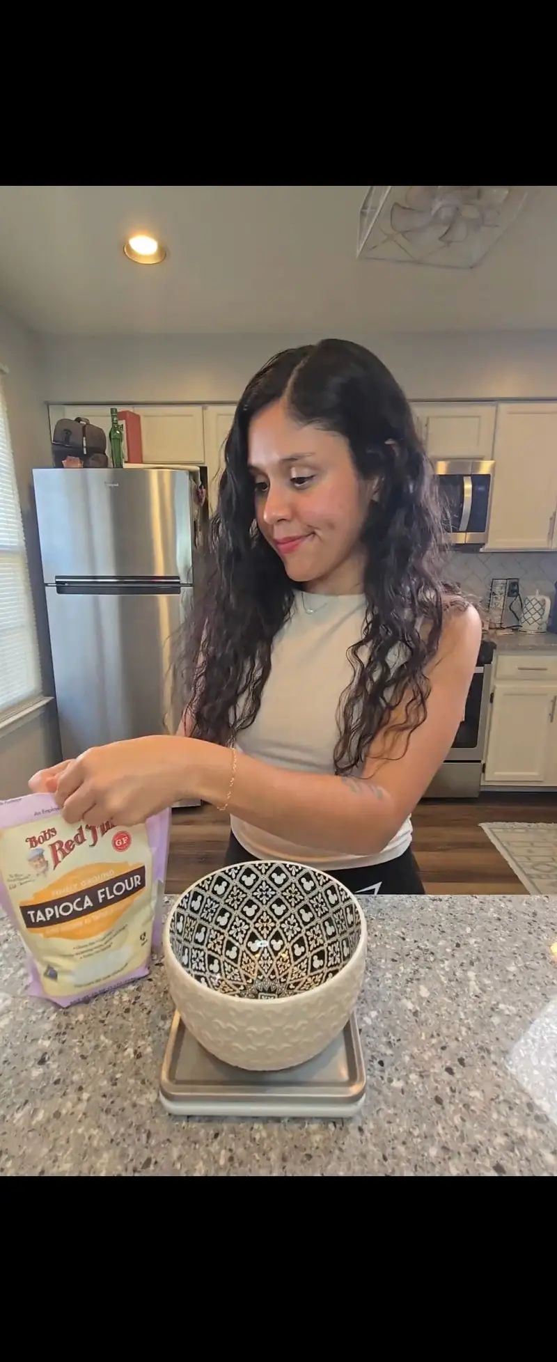 Crystal adding tapioca flour to a bowl of mashed sweet potato on the scale